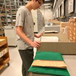 Young man standing looking at some volumes laid out on book cushions and foam supports in the archive Store