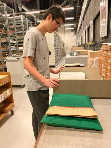 Young man standing looking at some volumes laid out on book cushions and foam supports in the archive Store