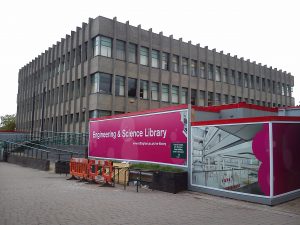 Photograph of the exterior of George Green Library with construction boards in front of it and an artistic depiction of what the interior will look like once completed.