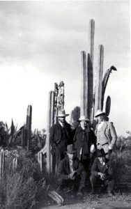 D.H. Lawrence, Frieda Lawrence and Witter Bynner standing in front of a cactus at Orizaba, Mexico with two native Mexicans crouching in front. The photograph was probably taken by Willard Johnson, in 1923.
