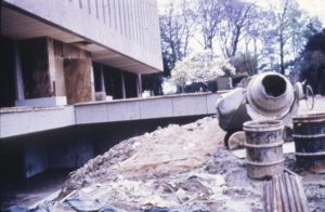 Photograph showing building site, including barrels and cement mixture, with the bridge to the library building entrance seen in the background.