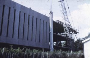 Photograph showing exterior of library building with a tall horizontal concrete panel being lifted by a crane to be fixed into place on the side of the building.
