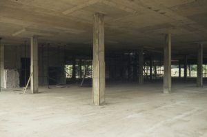 Photograph showing the hollow interior of a building under construction, showing concrete floor and ceiling with bare columns.