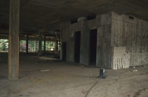 Photograph showing hollow interior of a building during construction with concrete floor and ceiling. There are also two dark, door-like openings within an internal concrete cube in the middle of the floor.