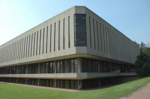 Photograph showing the external corner of the library, two sides of the grey concrete walls, with tall thin slit windows.