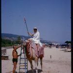 A colour photograph of a man riding a camel on the beach at Varna, Bulgaria