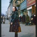 A photograph of a woman in traditional Slavic clothing standing on an urban street.