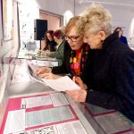 Photograph of women comparing documents with the display case contents.