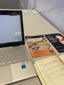 Items on a desk including laptop, printed flyers and notebook