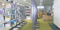 Photograph showing book stacks and a library lending desk.