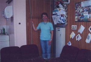 Photograph of Tracey O'Sullivan posing next to a wooden hatch in a wall and holding a rope.