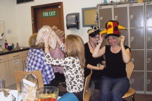 Photograph showing library staff members grabbing colourful hats off each other's heads