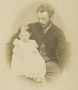 Black and white photograph of a man with an infant girl on his lap. 