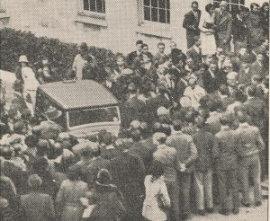 Photograph of a car surrounded by crowds of people