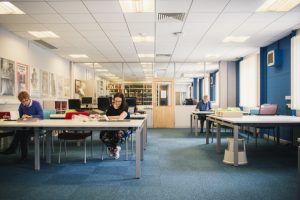 Colour image of three people reading books and manuscripts in the Reading Room.