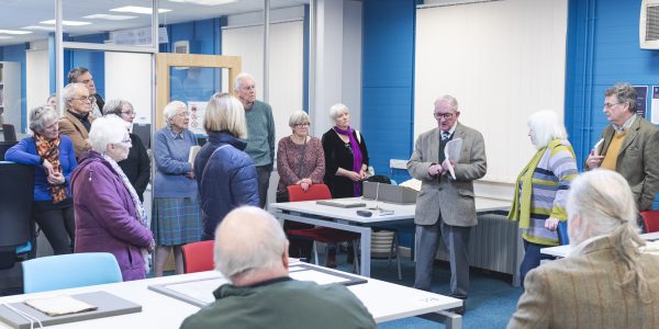 An image of a man standing in the Manuscripts and Special Collections reading room, giving a talk to a crowd of onlookers.