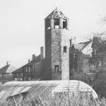 Black and white photo of tall hexagonal brick structure with openings at the top.