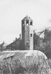 Black and white photo of tall hexagonal brick structure with openings at the top.