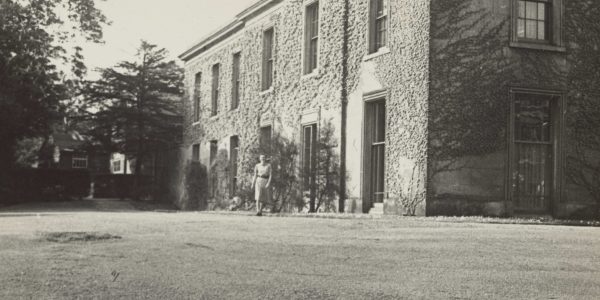 Black and white photograph of large two-storey house surrounded by grass.