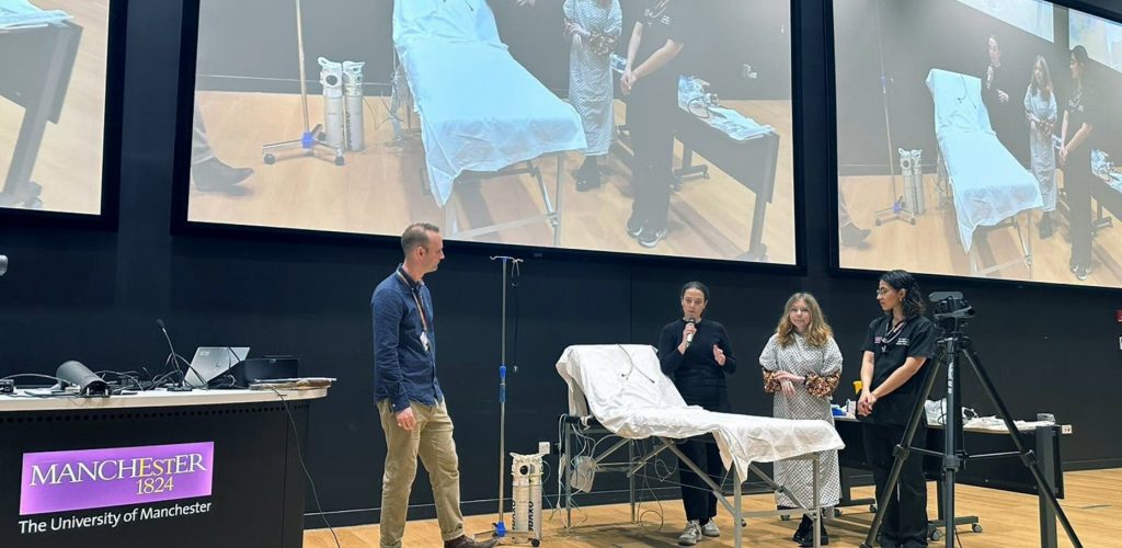 photo of man in front of large screen with actor patient and hospital bed