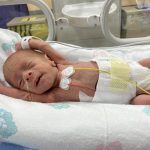 Premature baby covered in wires stretching in his crib