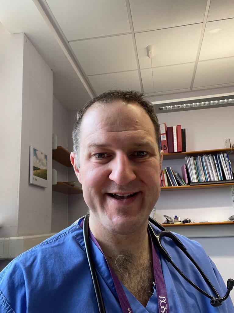 Professor Adam Gordon smiling at the camera in his medical scrubs