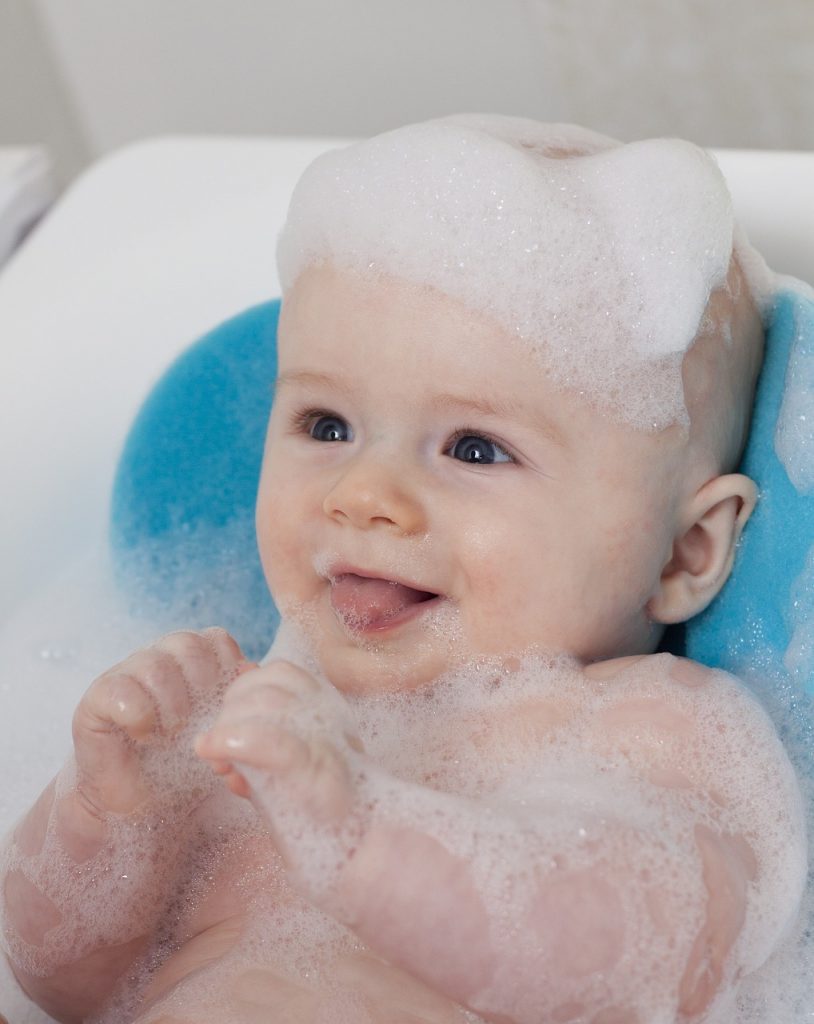A baby covered in soap suds in a bath