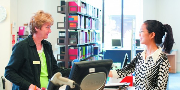 Information assistant handing books to a female undergraduate student, James Cameron-Gifford Library, Sutton Bonington campus