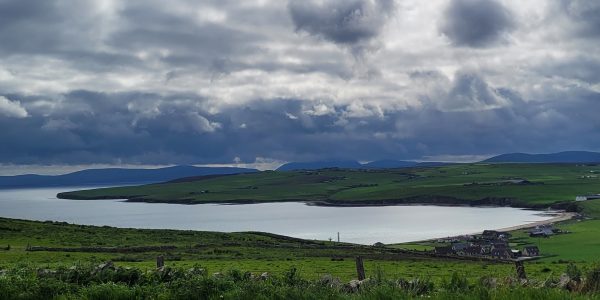 Photograph taken looking down to the bay of Scapa, a deeply curved bay, surrounded by farm land.