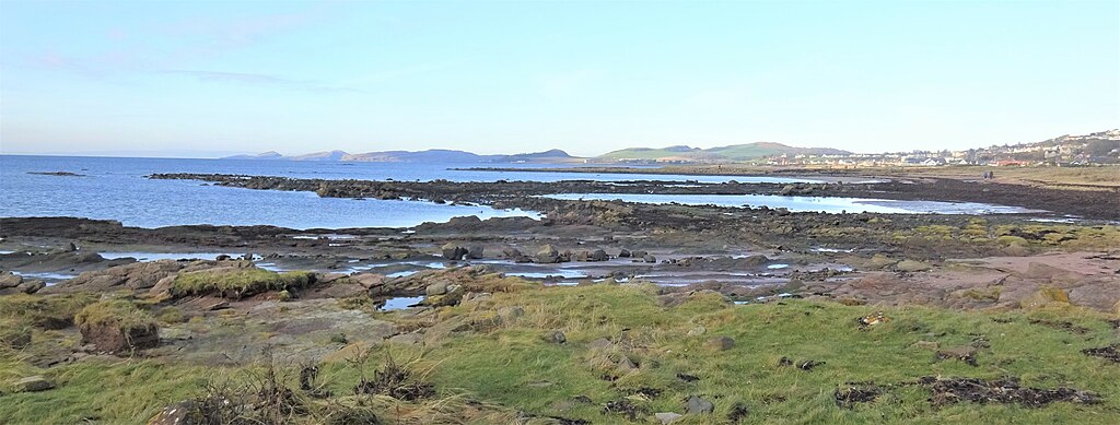 Photograph of a coastal bay with the tide out exposing a circular rock formation in which fish would be trapped at low tide.