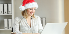 A woman managing her workload at her laptop wearing a read Christmas hat