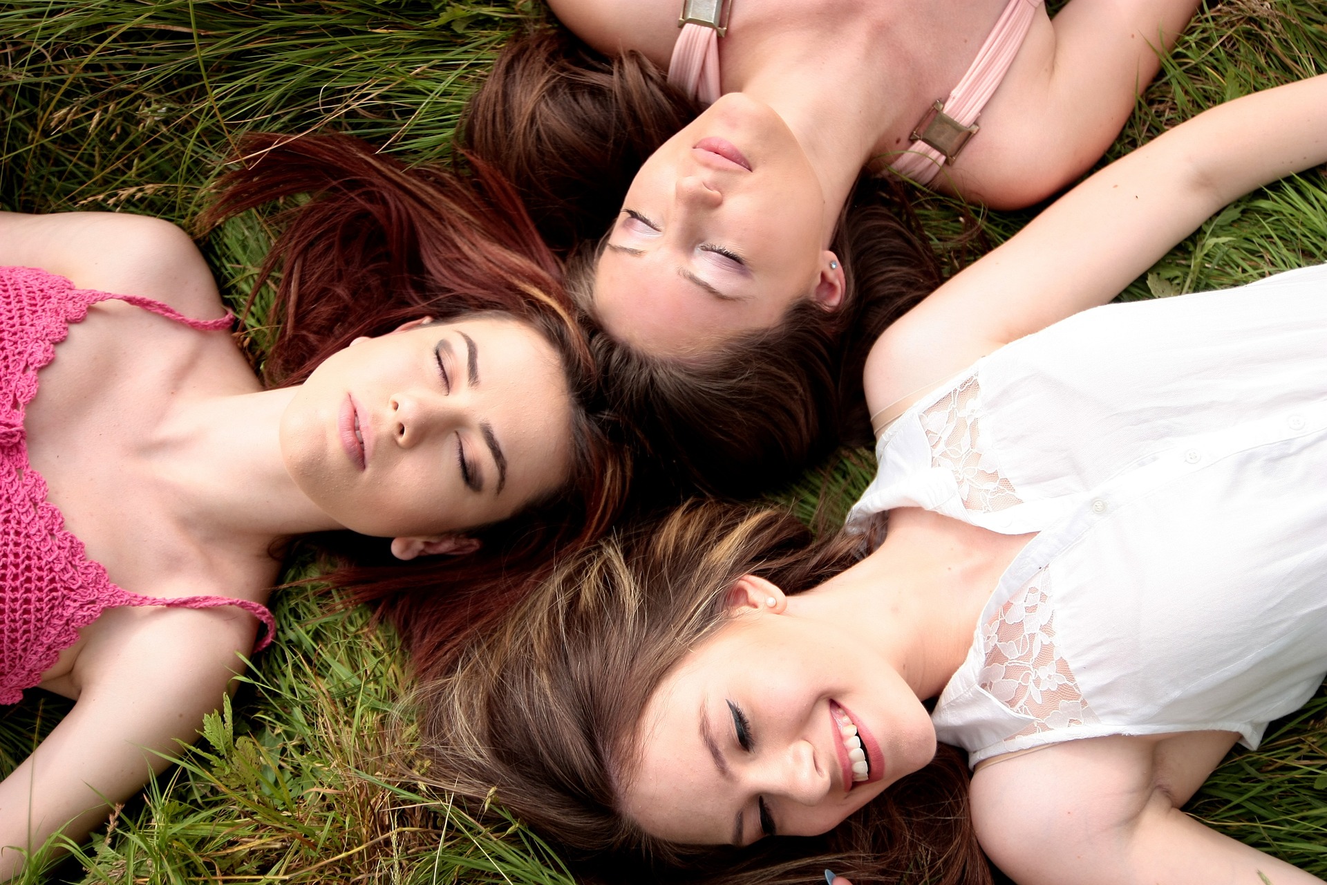 Three women laying on the grass with their eyes closed