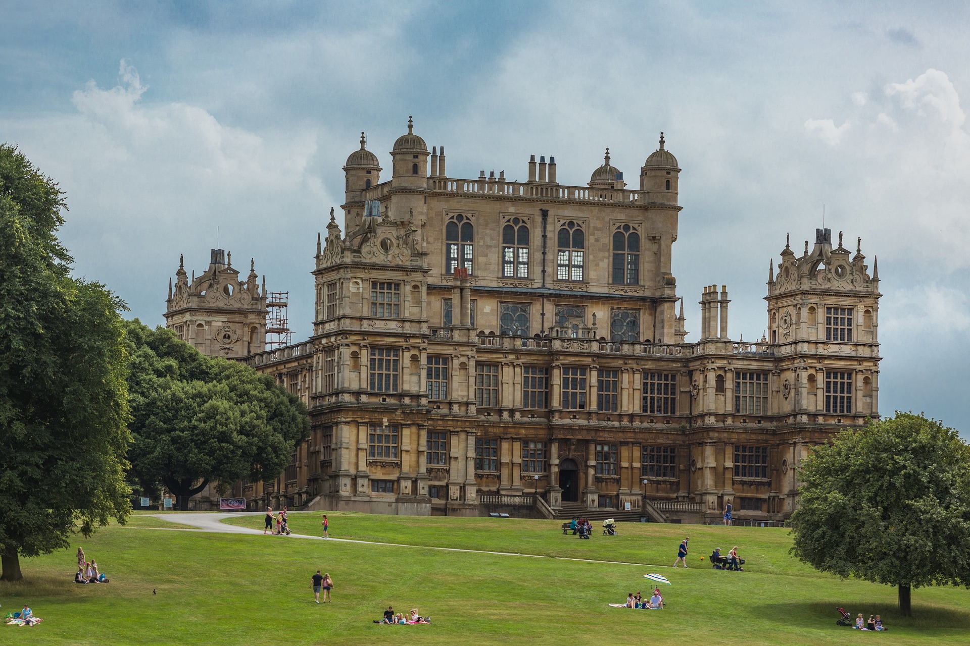Groups of people sat down outside Wollaton hall on the green lawn.