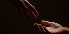 Two hands reaching for each other on a dark background.