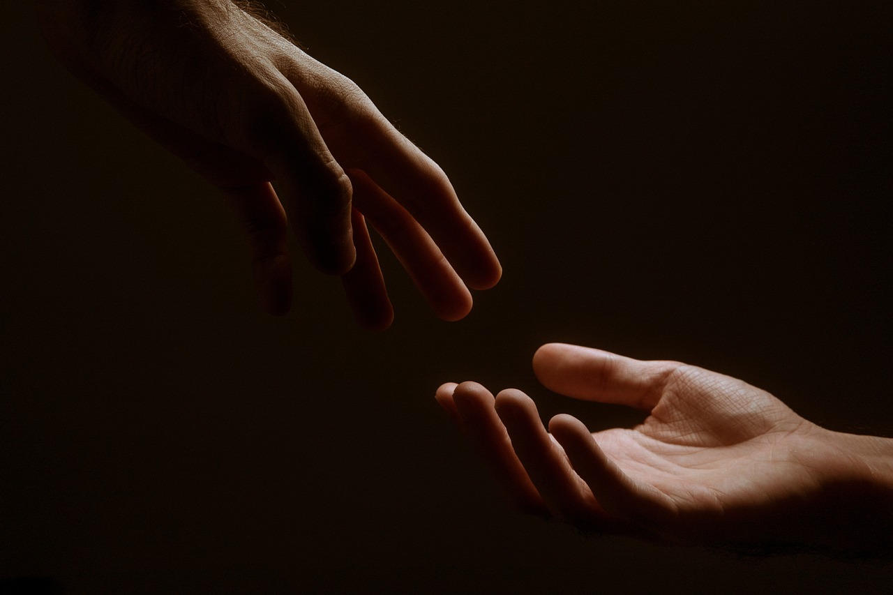 Two hands reaching for each other on a dark background.