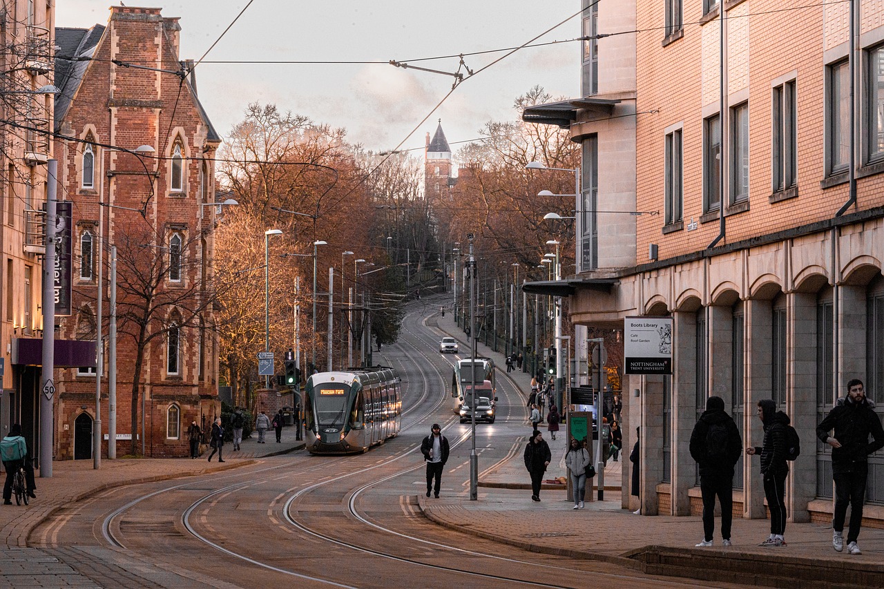 An image of a street in Nottingham at sunset, depicting a tram and people on the street.