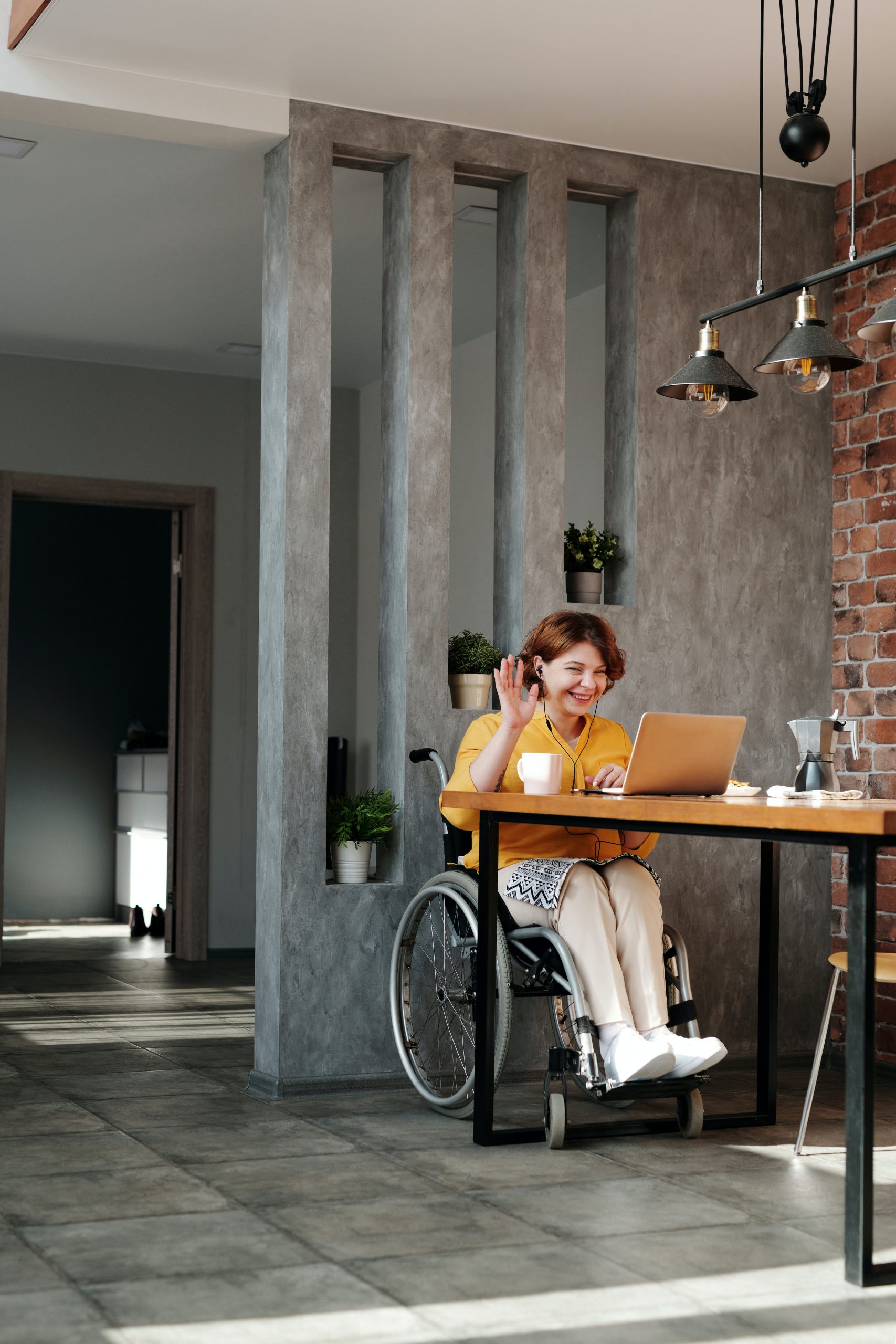 A person on a wheelchair sitting and smiling in front of their laptop on a meeting, potentially connecting with a group