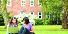 Two female students sitting with laptop outside