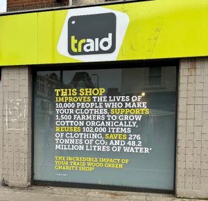 The windowfront of a Traid store featuring text 'This shop improves the lives of 10,000 people who make your clothes, supports 1,500 farmers to grow cotton organically, reuses 102,000 items of clothing, saves 276 tonnes of CO2 and 48.2 million litres of water'
