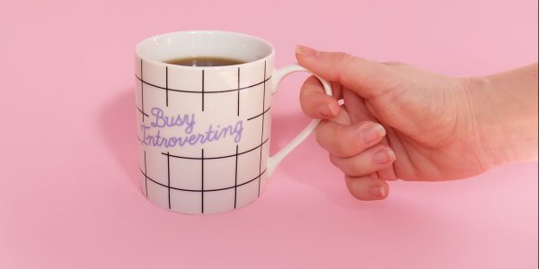 A hand holding a mug that reads 'busy introverting'.