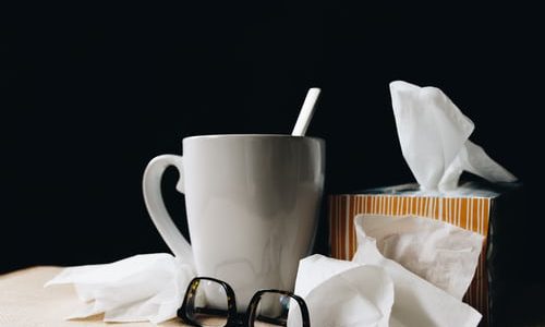 A mug, open tissue box and glasses on a desk