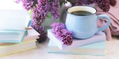 A mug of tea on a pile of books, with pink flowers in the background