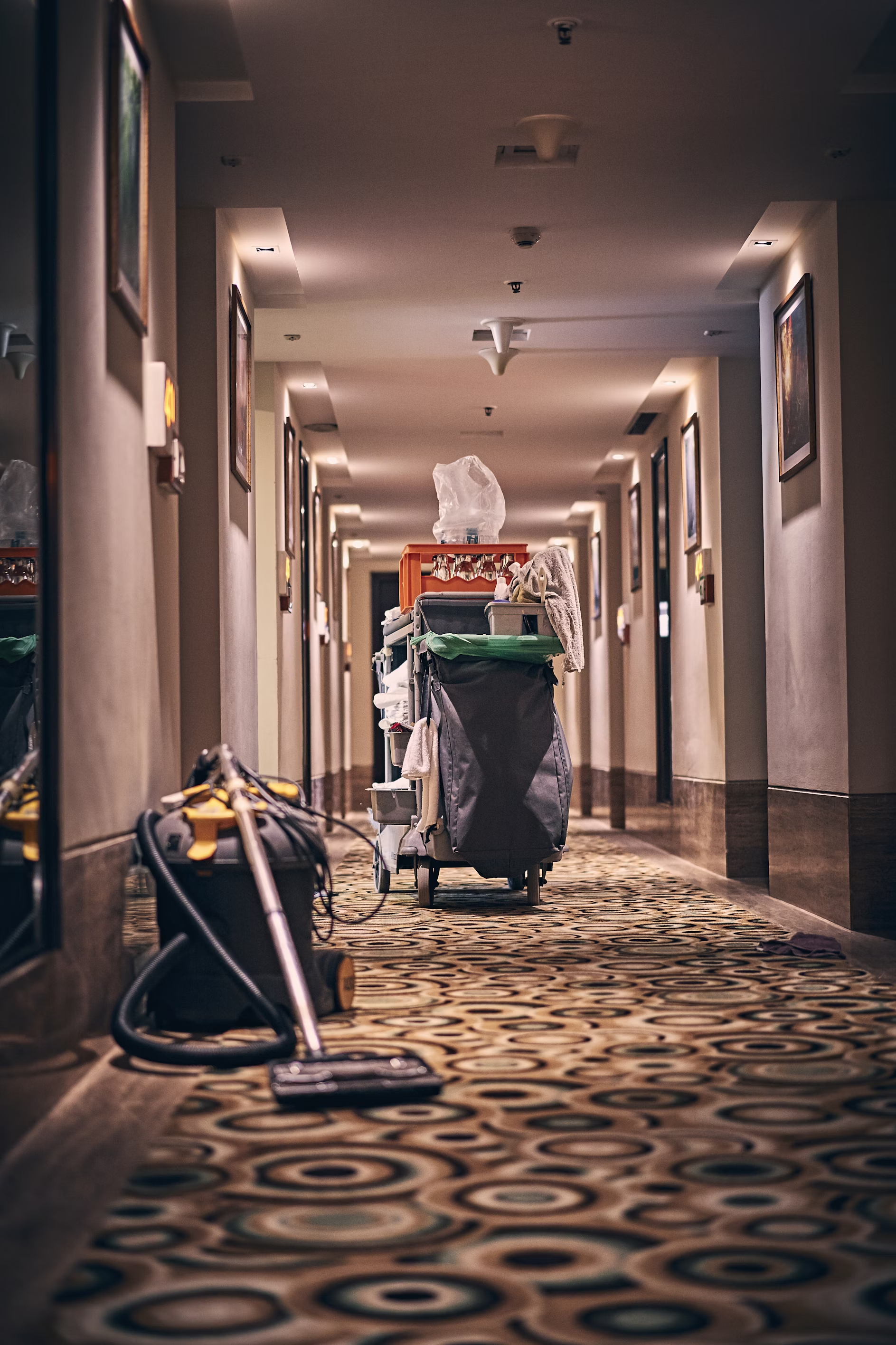 An empty corridor with a cleaning cart and vacuum cleaner in the middle.