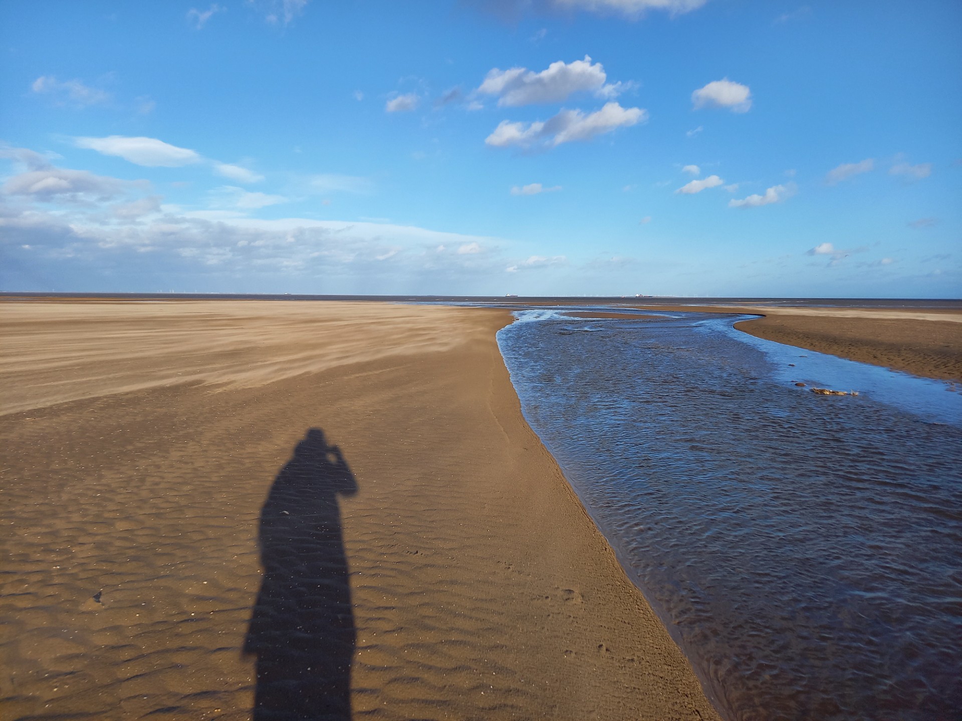 A beach with a person's shadow visible on the sand.